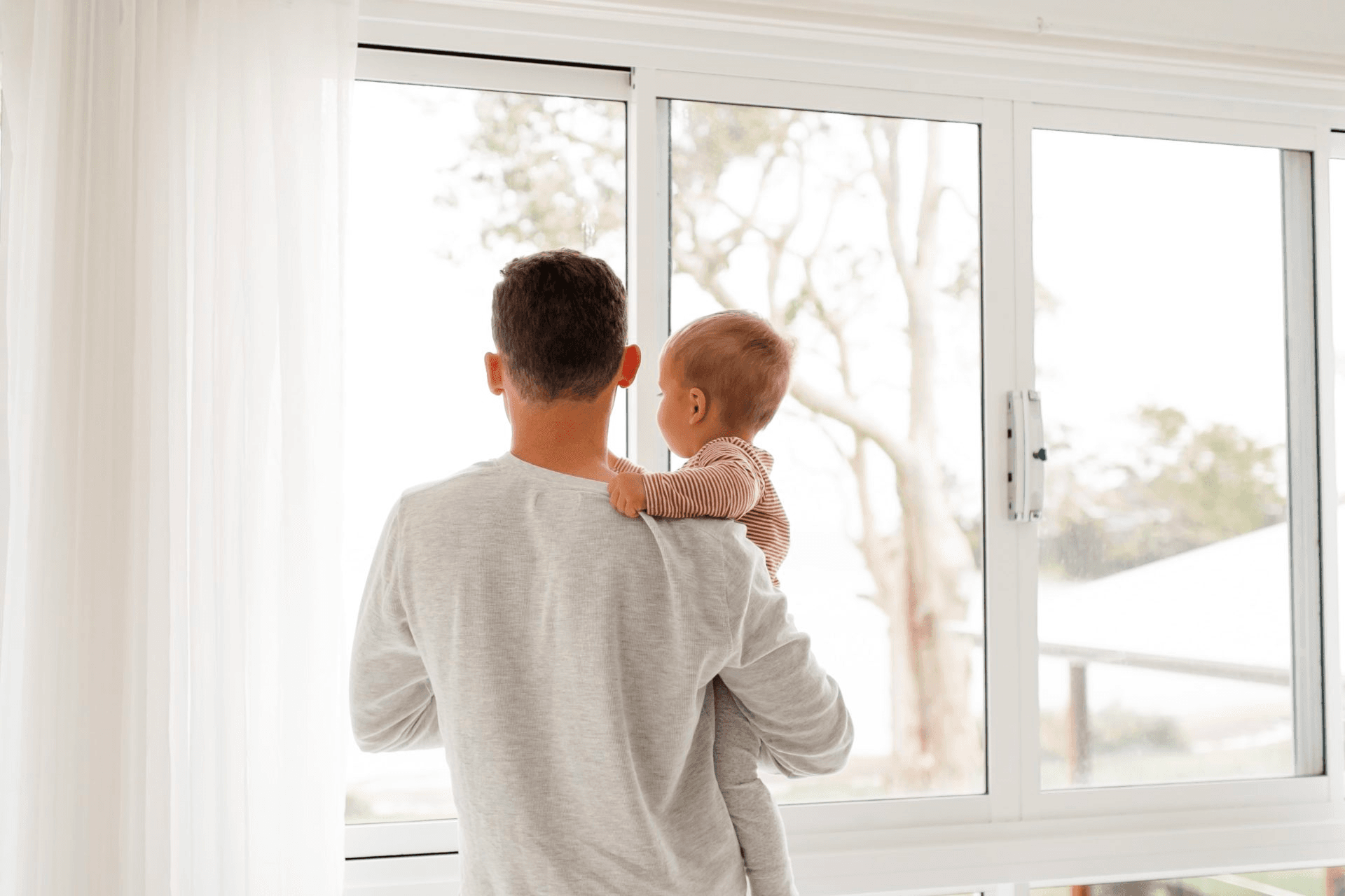 Man holding baby in front of window