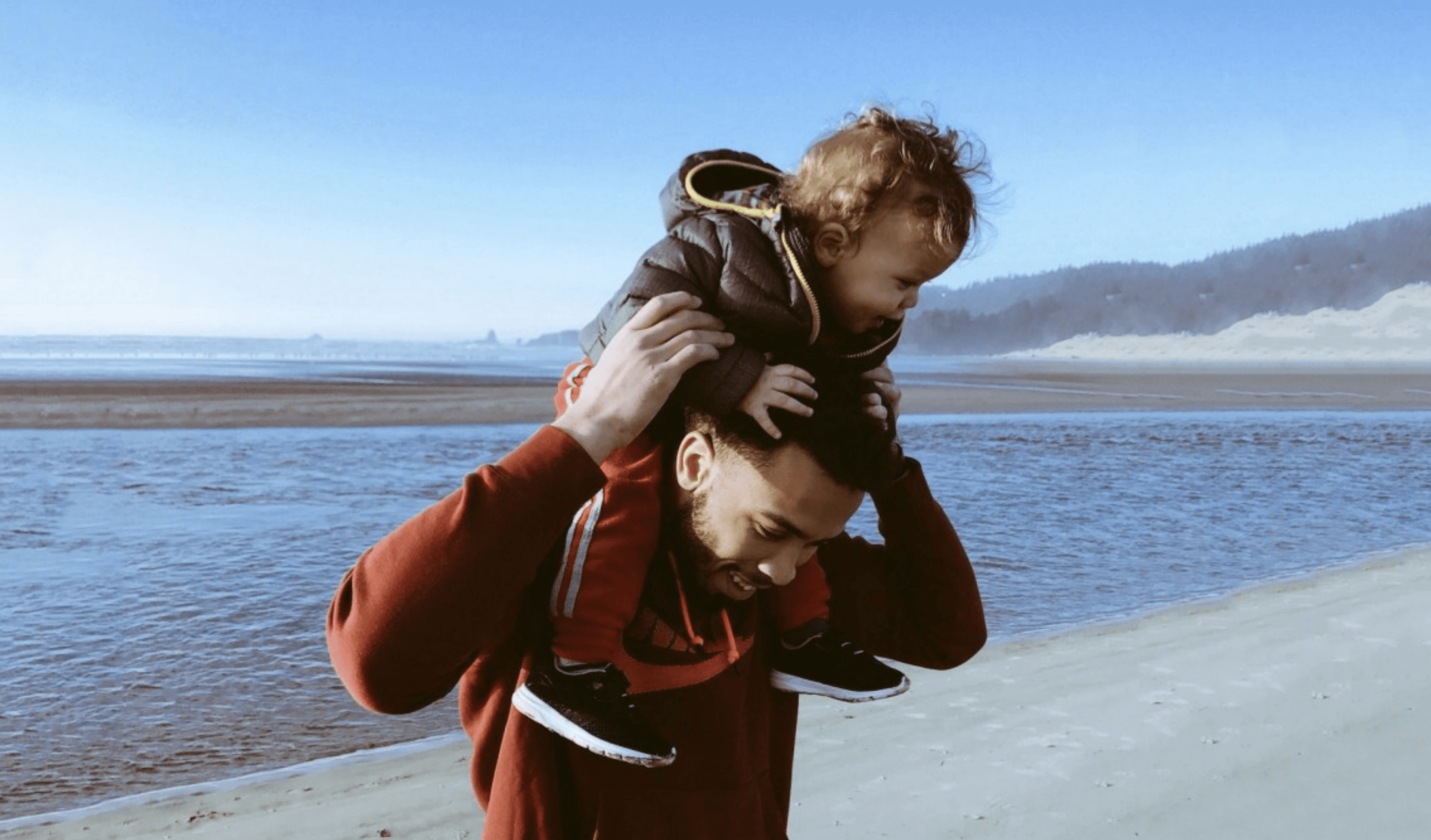Young man holding young child on head at beach